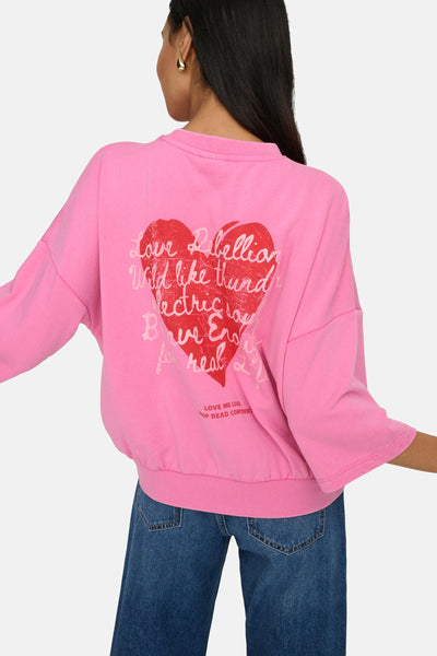 Sweat rose de ONLY® avec un imprimé cœur et slogan au dos, porté avec un jean taille haute.