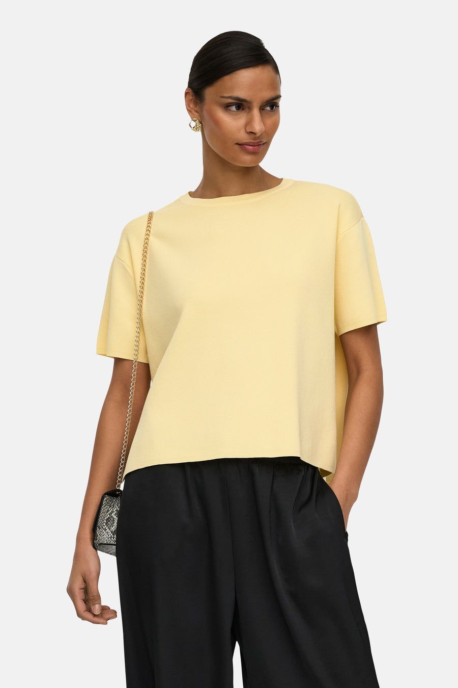 Pull jaune à col rond de JDY, porté avec un pantalon noir fluide et un sac à chaîne.