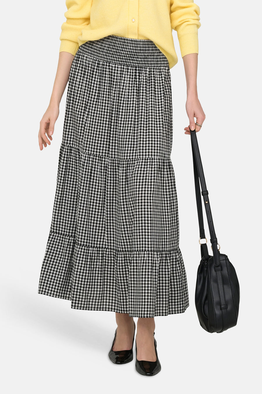JDY lange meerkleurige rok, zwart-wit geruit, met ruches, gedragen met een gele cardigan en zwarte pumps.