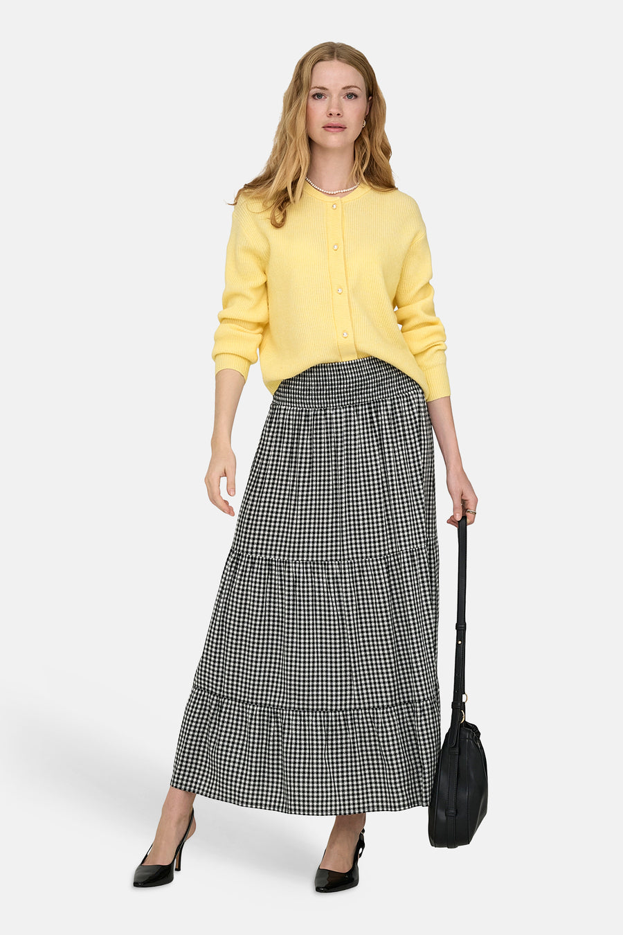 Jupe longue multicolore de JDY, à carreaux noirs et blancs, coupe à volants, portée avec un cardigan jaune et des escarpins noirs.