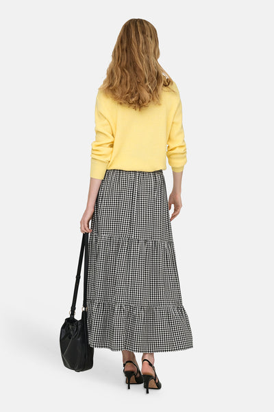 Jupe longue à carreaux noire et blanche de JDY, portée avec un pull jaune, avec un sac à main noir et des talons noirs.