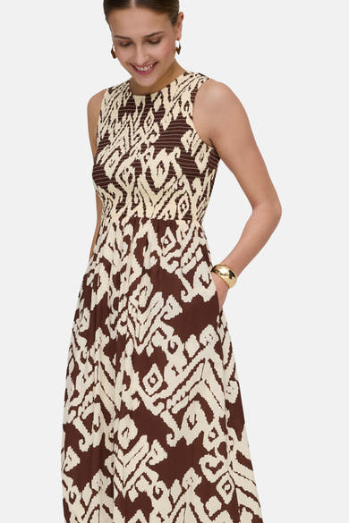 Multikleurenjurk van JDY met bruin en beige abstract patroon, met een mouw in de zak en een gouden armband.
