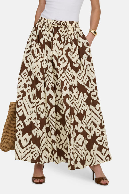 Jupe longue multicolore JDY, à motif abstrait, portée avec un haut blanc, un bracelet doré et un sac en paille.
