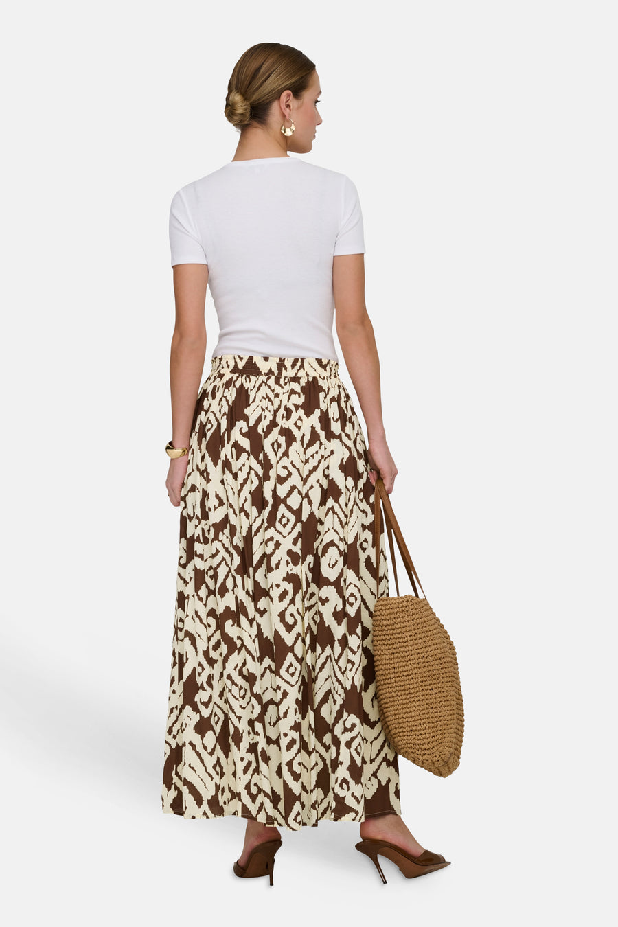 Lange meerkleurige rok van JDY, bruin en beige abstract patroon, gedragen met een wit T-shirt en een gevlochten tas.