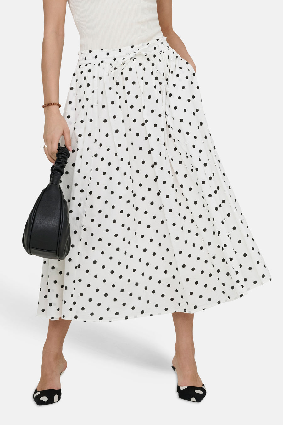 Jupe longue blanche à pois noirs de JDY, avec une ceinture nouée, portée avec un haut blanc et des mules assorties.

