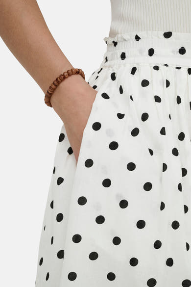 Jupe longue blanche à pois noirs de JDY, avec un poignet orné d'un bracelet en perles.
