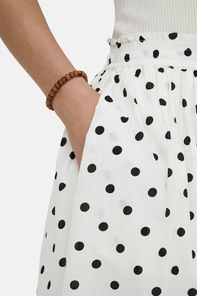 Jupe longue blanche à pois noirs de JDY, avec un poignet orné d'un bracelet en perles.