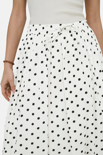 Jupe longue blanche à pois, par JDY, avec ceinture nouée et bracelet marron.
