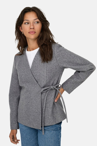 Veste courte grise de ONLY, avec ceinture nouée, portée sur un t-shirt blanc et un jean bleu.