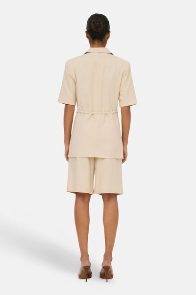 Beige Bermuda van JDY, van achteren gezien met een bijpassend kort jasje met riem en hakken.