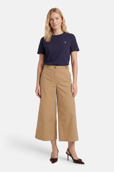 Beige wide-leg cropped pants with front pockets and button waist, worn with navy t-shirt and brown heels, full-length front view
