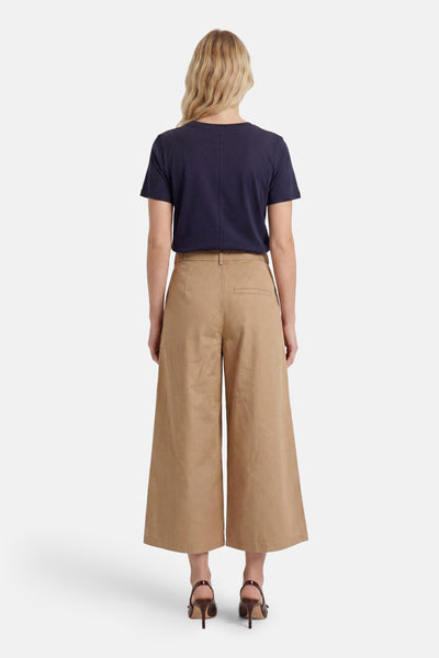 Beige wide-leg trousers from back view, featuring high waist, single back pocket, and cropped length on model wearing navy top and brown heels