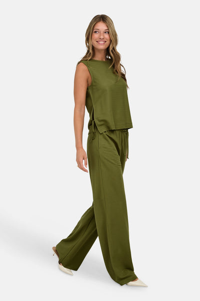 Olive green sleeveless blouse with side ties and relaxed fit, worn with matching wide-leg pants and white pointed-toe heels, side view.