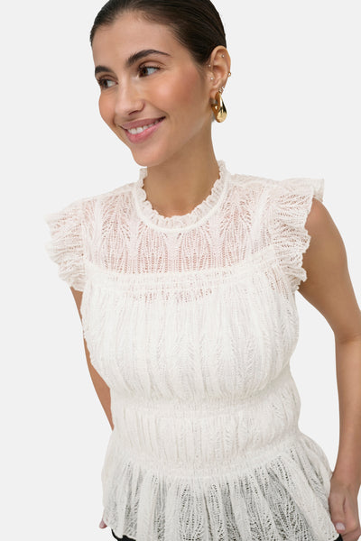 White sleeveless knit top with ruffled cap sleeves and smocked bodice, featuring a textured lace pattern and flared hem, shown in front view on model.