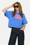 Blauwe trui van ONLY, met een roze "Girl Club" print, gedragen met een donkere flared jeans en een zonnebril.