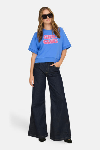 Sweat-shirt bleu de ONLY, avec un motif "Girl Club" rose, porté avec un jean évasé foncé et des lunettes de soleil.