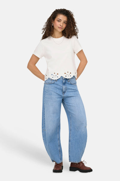 T-shirt blanc à manches courtes de ONLY® avec ourlet festonné ajouré, porté avec un jean large et des chaussures marron.