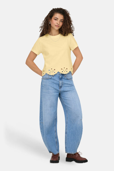 T-shirt jaune à manches courtes de la marque ONLY® avec ourlet festonné à découpes, porté par une femme avec un jean large.