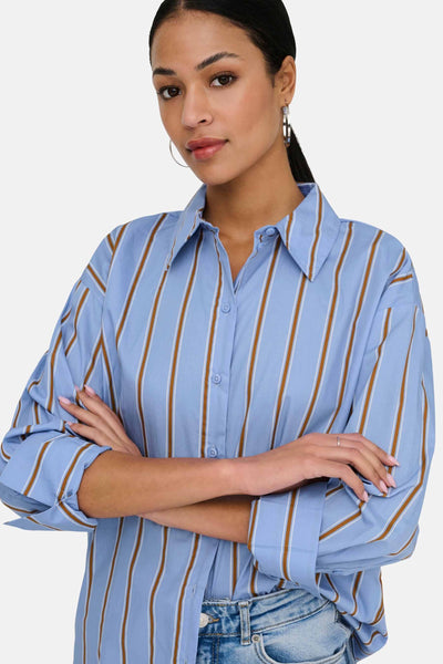 Light blue long-sleeve striped chemise with brown and white vertical stripes, button-down front, worn with rolled sleeves and paired with jeans.