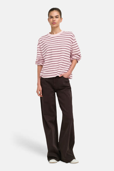 Pale lilac long-sleeve striped T-shirt with burgundy horizontal stripes, worn loose with rolled sleeves and paired with dark wide-leg pants and white shoes.