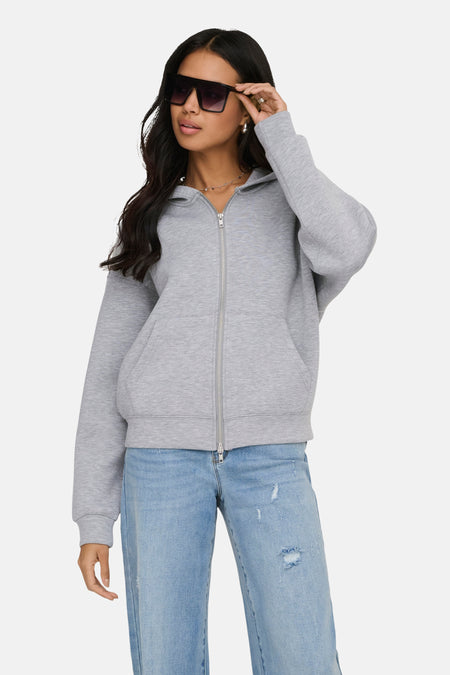 Gilet gris zippé de ONLY, porté avec un jean bleu délavé et des lunettes de soleil noires.