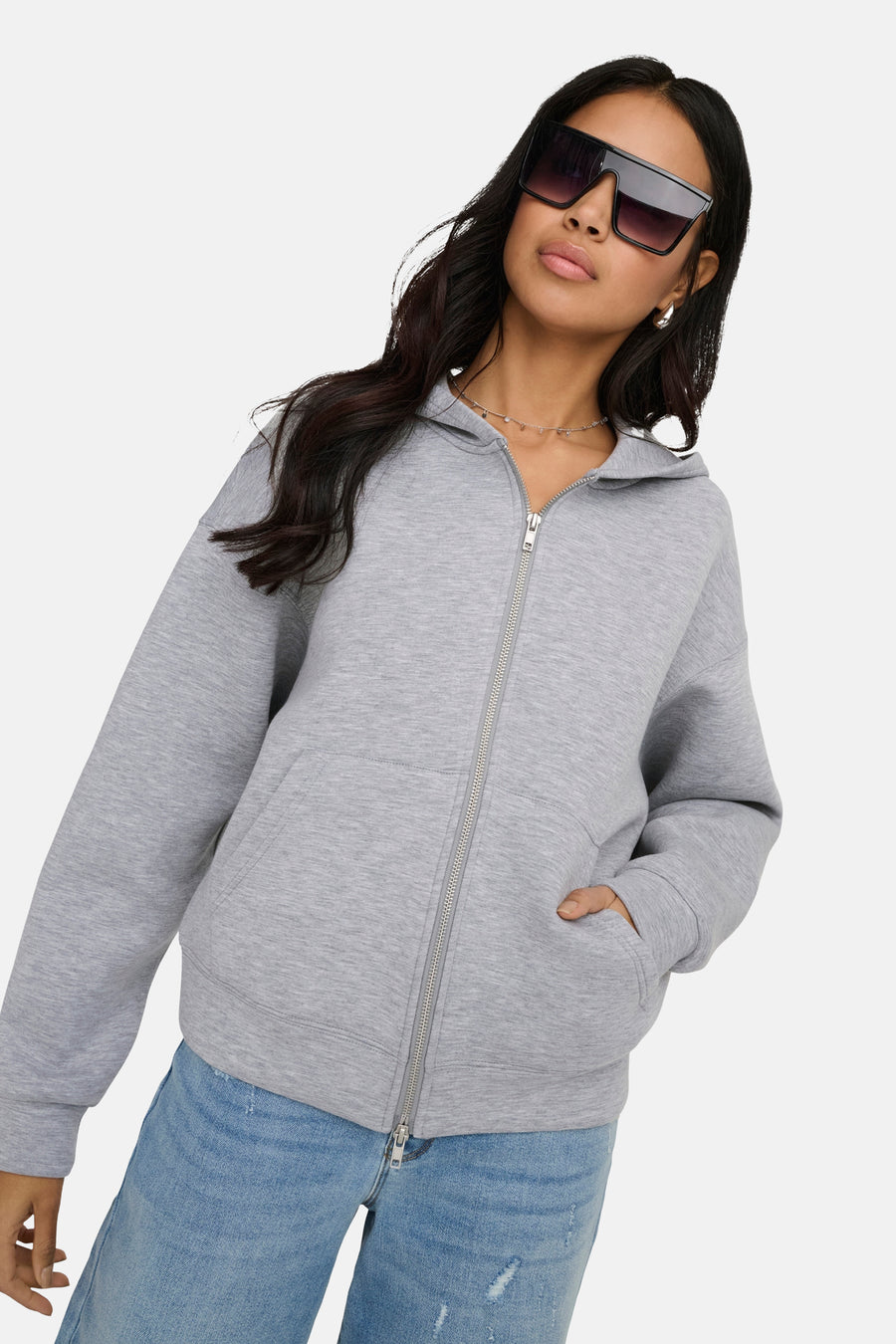 Gilet gris par ONLY, avec fermeture éclair et poches, porté avec des jeans et des lunettes de soleil oversize.