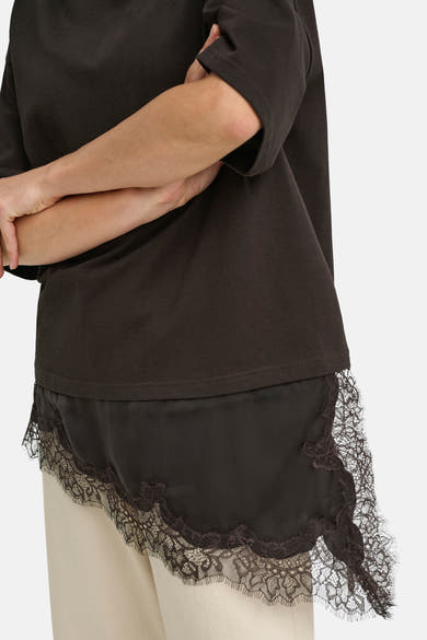 Dark brown short-sleeve t-shirt with lace-trimmed hem, side view, worn with light beige pants
