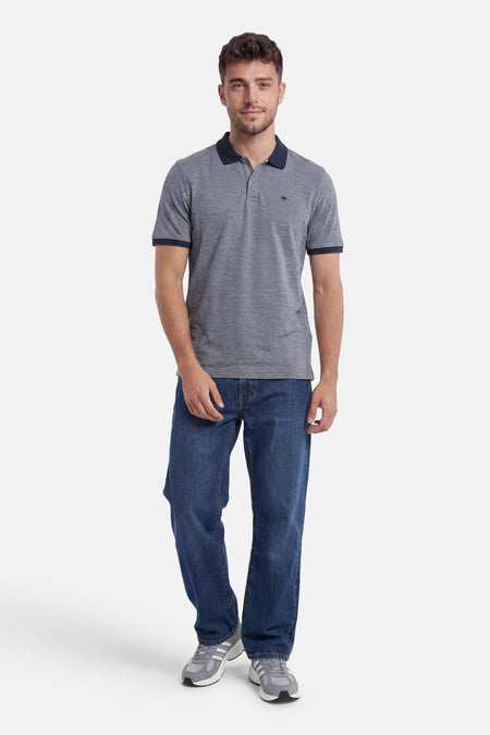 Polo bleu chiné de FYNCH-HATTON avec logo kangourou, col et bords de manches marine, porté avec un jean.