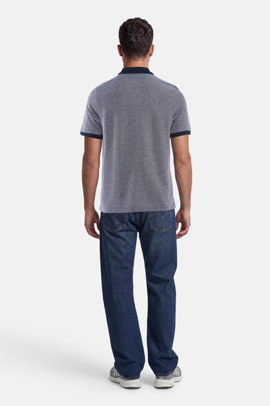 Polo bleu de FYNCH-HATTON à micro-motif, col et bordures des manches marine, vue de dos sur un homme en jean.