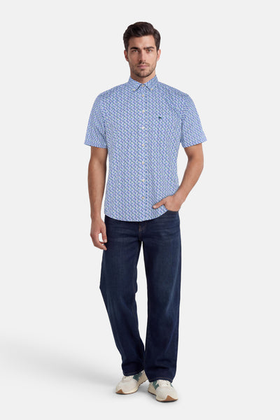 Chemise à manches courtes multicolore de FYNCH-HATTON avec motif de petites baleines bleues et vertes, portée par un homme avec un jean foncé et des baskets crème et vertes.