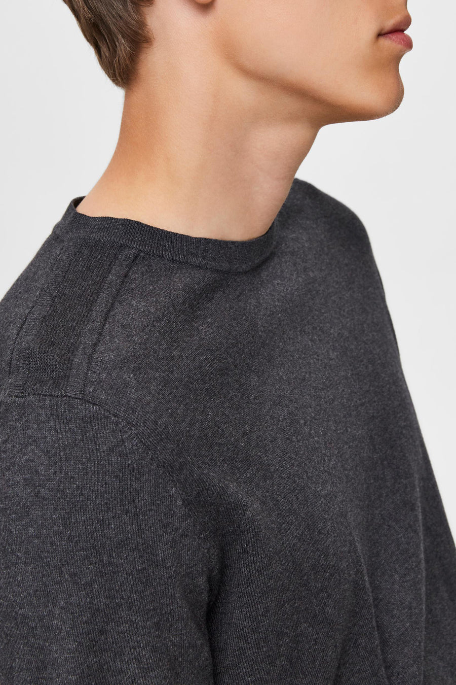 Pull gris en maille par SELECTED, détail de couture à l'épaule, porté par un homme, en vue rapprochée.
