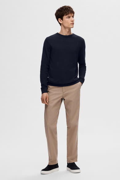 Pull bleu de SELECTED, porté avec un pantalon chino beige et des chaussures décontractées noires.
