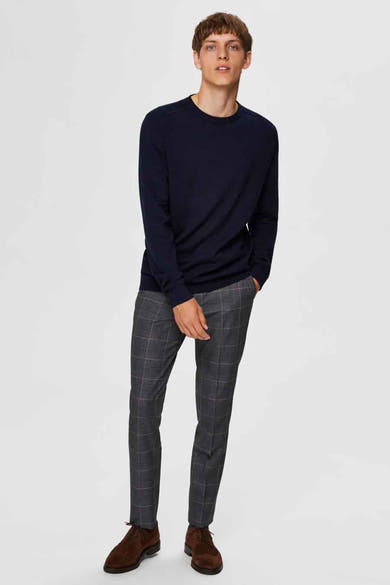 Pull col rond bleu de SELECTED, porté avec un pantalon à carreaux et des chaussures en daim marron.