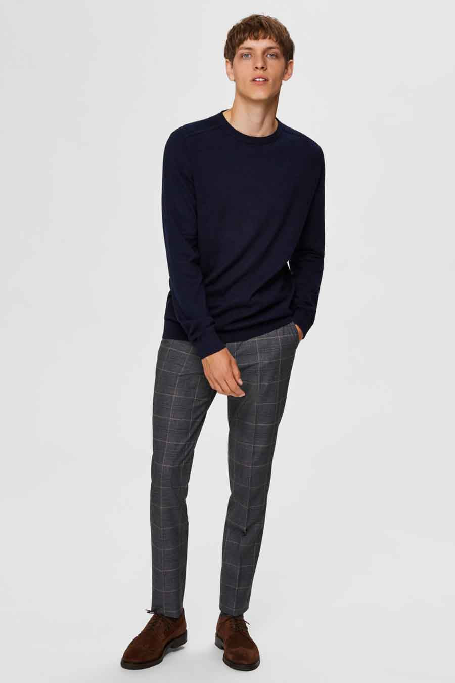 Pull col rond bleu de SELECTED, porté avec un pantalon à carreaux et des chaussures en daim marron.