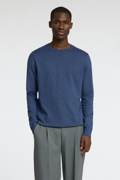 Pull ras du cou bleu de SELECTED, porté avec un pantalon gris à plis.