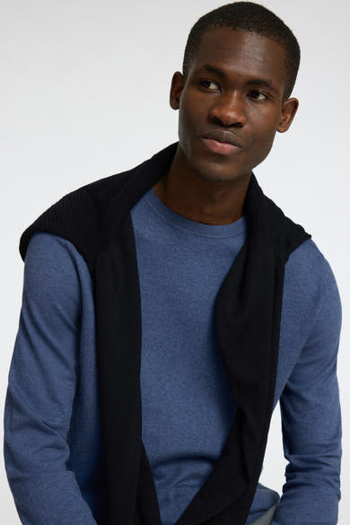 Pull à col rond bleu par SELECTED, avec un pull noir nonchalamment posé sur les épaules.
