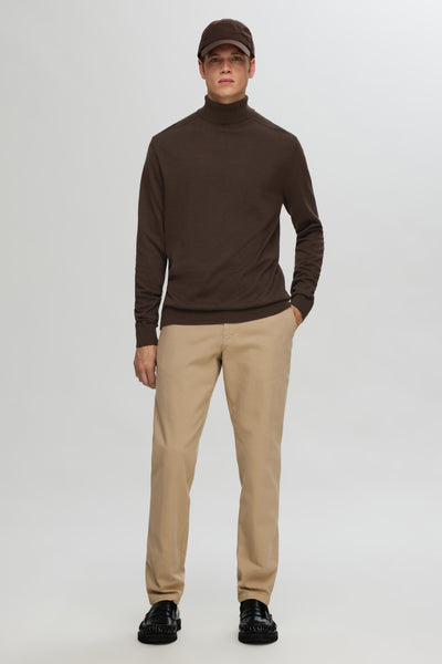 Pull à col roulé brun de SELECTED, porté avec un pantalon beige et des mocassins noirs.
