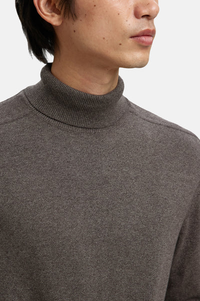 Pull à col roulé brun de SELECTED, texture fine et uniforme, porté avec le col montant relevé.
