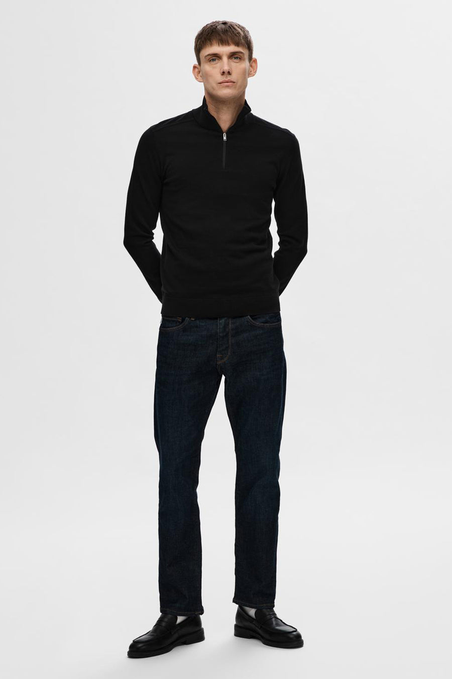 Pull noir par SELECTED, porté avec un jean bleu foncé et des mocassins noirs.