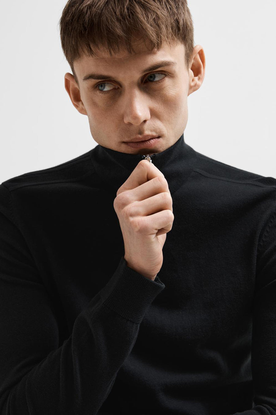 Pull noir de SELECTED, avec fermeture à glissière au col, porté par un homme regardant sur le côté.
