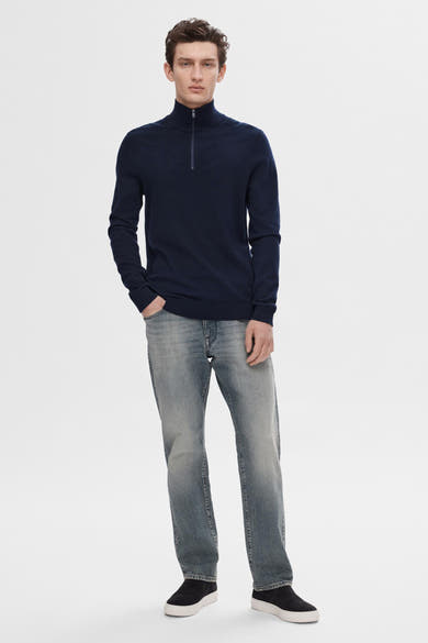 Pull bleu de SELECTED, porté avec un jean délavé et des chaussures de sport noires à semelles blanches.