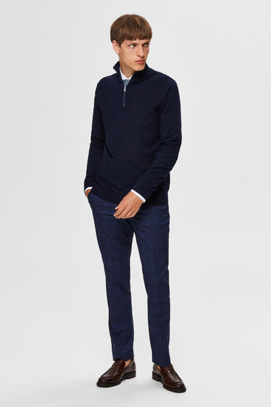 Pull bleu SELECTED avec fermeture éclair, porté avec une chemise blanche, un pantalon à carreaux et des chaussures marron.