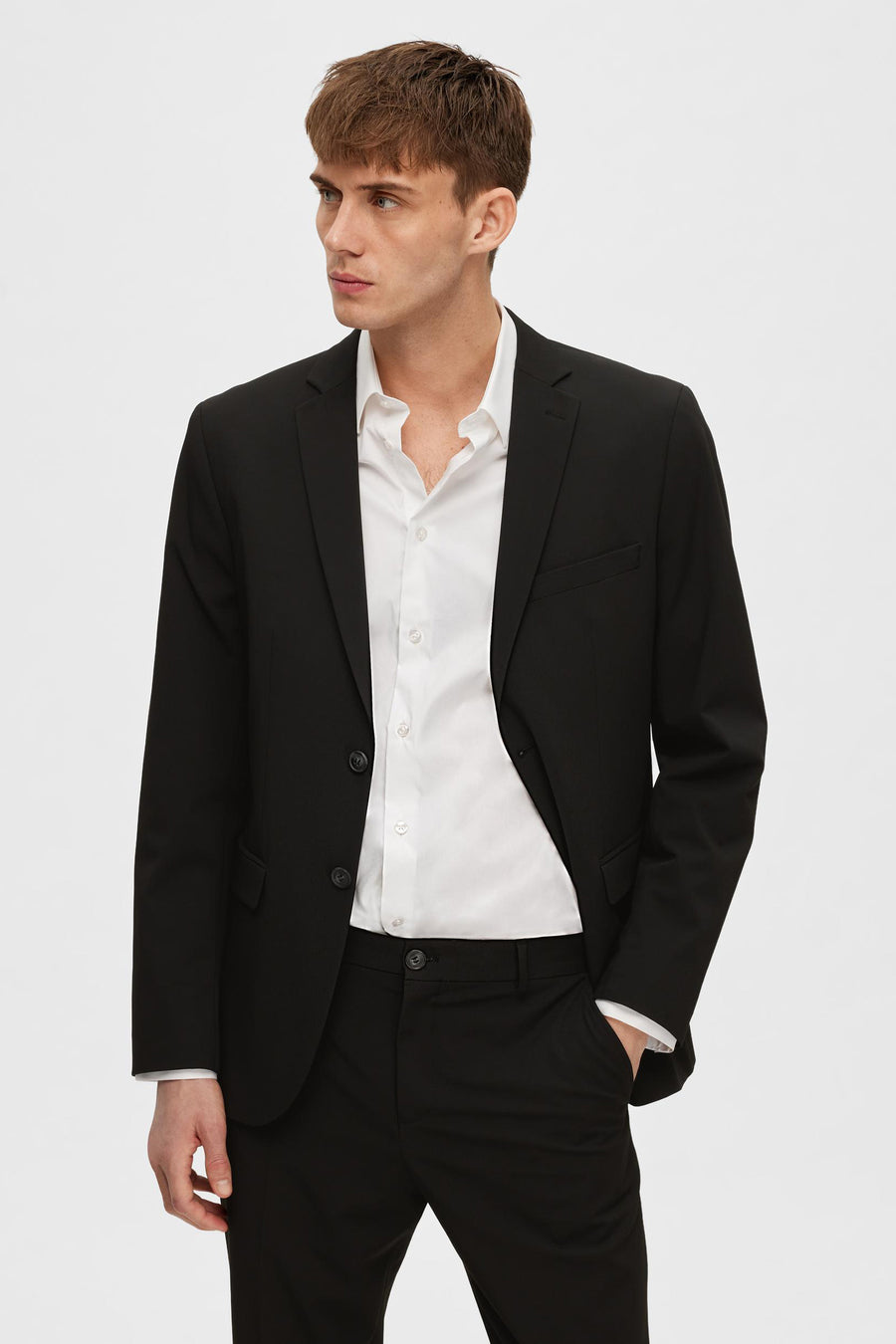 Zwarte blazer van SELECTED, gedragen over een open wit overhemd, met één hand in de zak.