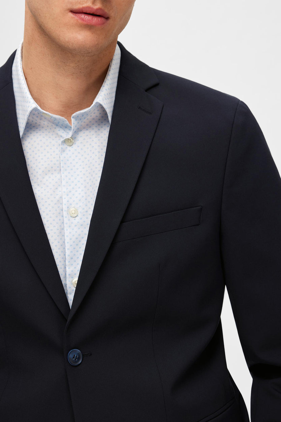Blazer bleu de SELECTED, avec une chemise blanche à motifs bleus et un bouton bleu assorti.