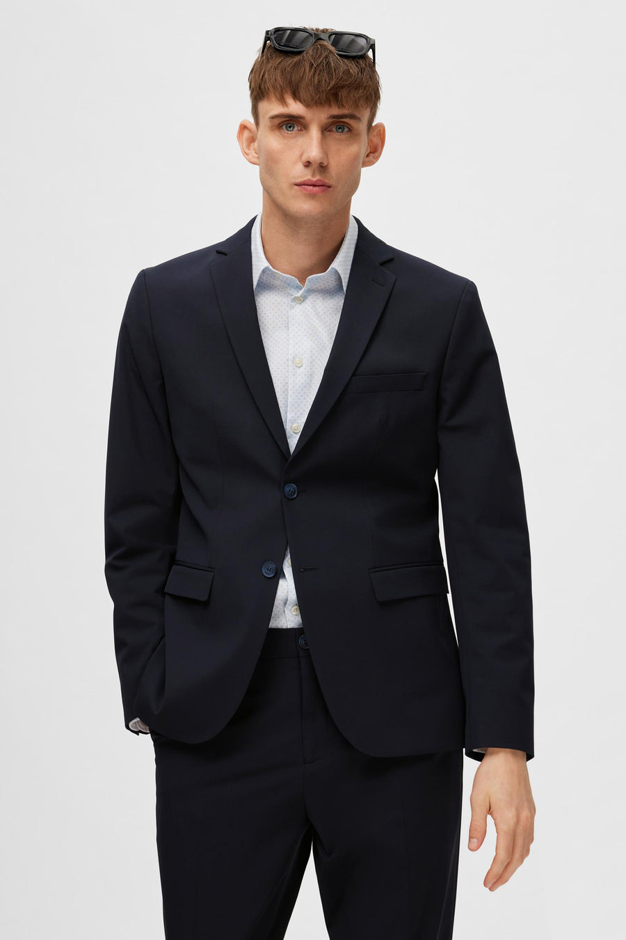 Blazer bleu marine par SELECTED, porté avec une chemise à motifs discrets et des lunettes de soleil sur la tête.