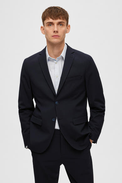 Blazer bleu marine de SELECTED, porté sur une chemise à motif discret, avec les mains dans les poches.