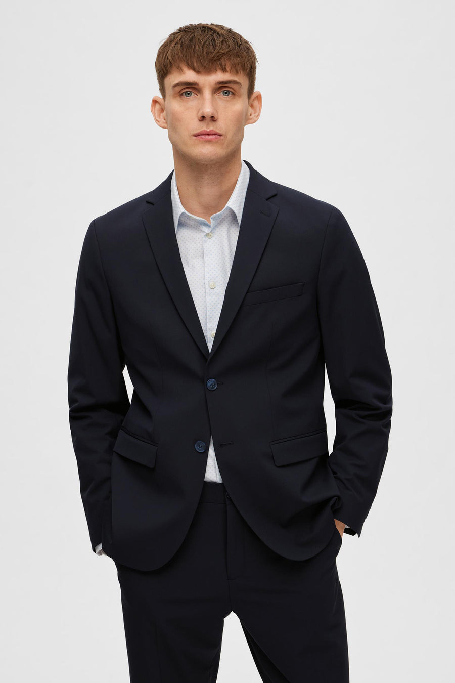 Blazer bleu marine de SELECTED, porté sur une chemise à motif discret, avec les mains dans les poches.