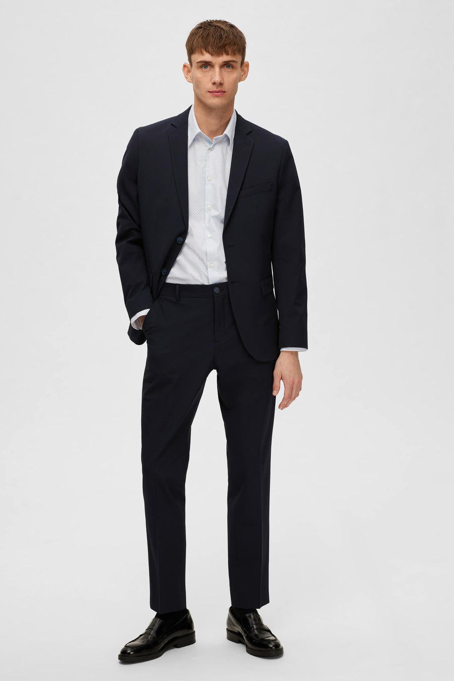 Blazer bleu de SELECTED, porté avec une chemise à motif et des chaussures noires classiques.