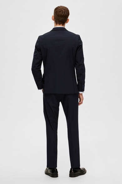 Blazer bleu marine de SELECTED, avec des manches longues, porté avec une chemise blanche et un pantalon assorti.