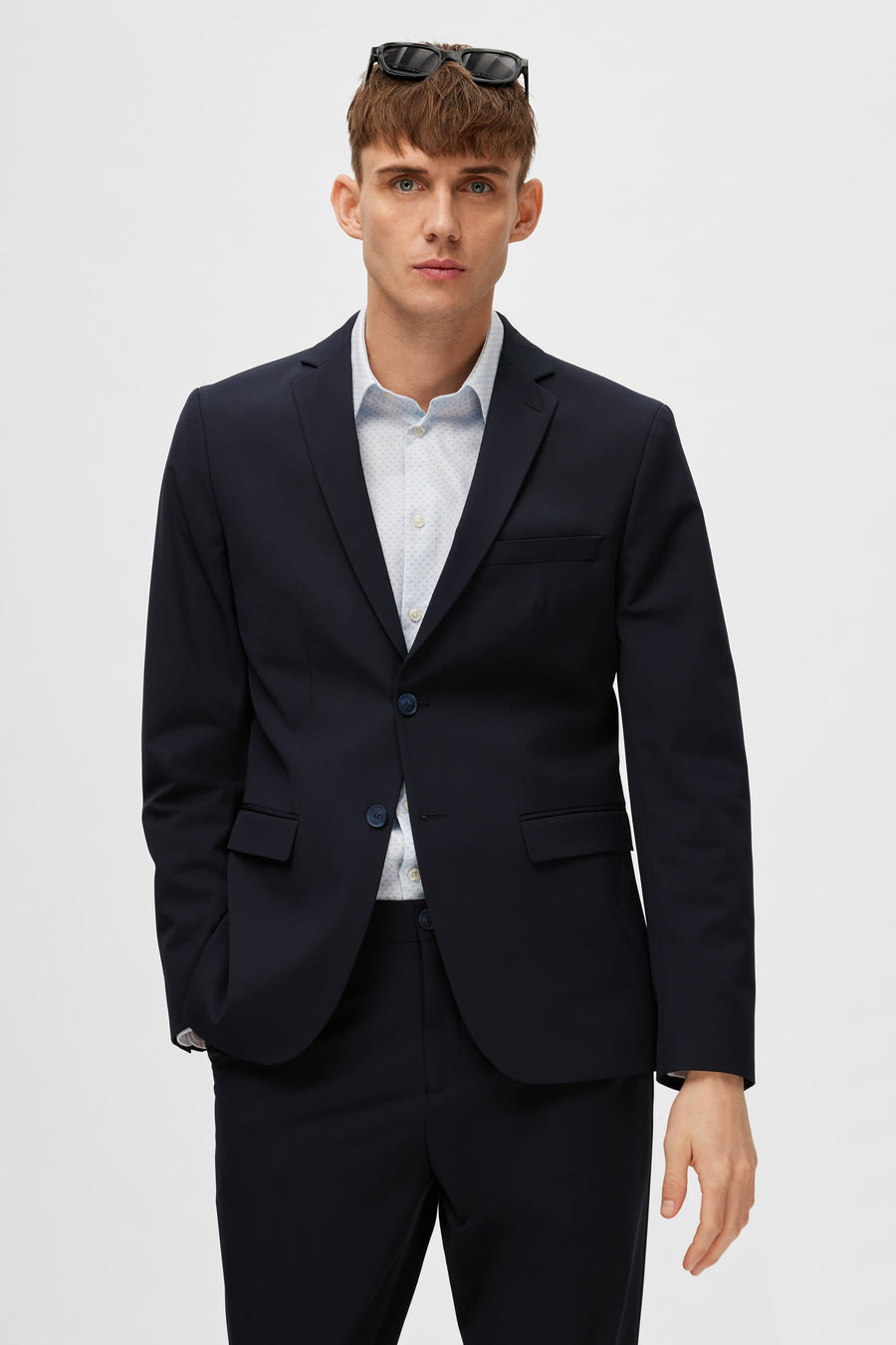 Blazer bleu de SELECTED, porté avec une chemise à motifs discrets et des lunettes de soleil sur la tête.
